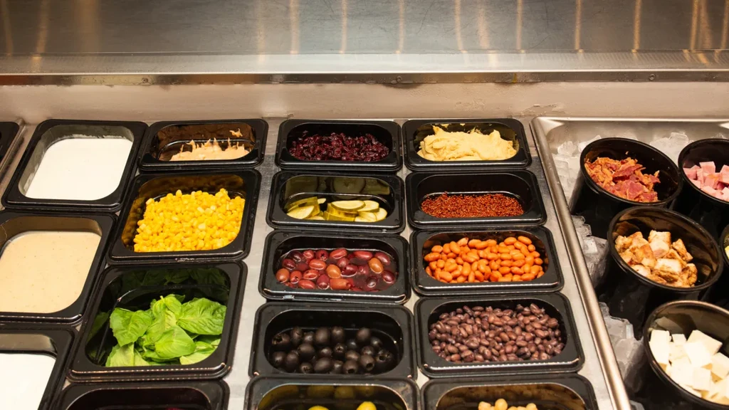 Well-stocked salad bar with fresh vegetables, dressings, meats, and cheese.