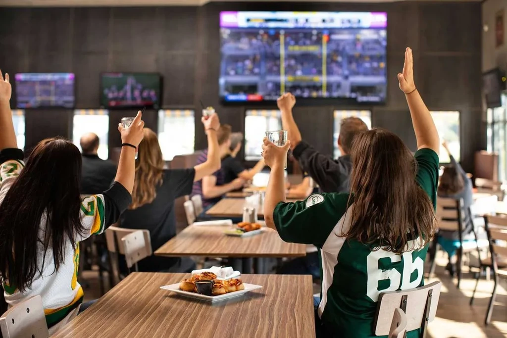 Sports fans celebrating a game in a bar with food and drinks.