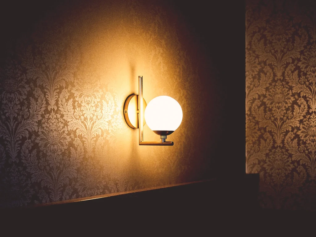 Contemporary gold sconce illuminates damask wallpaper with soft, warm light.