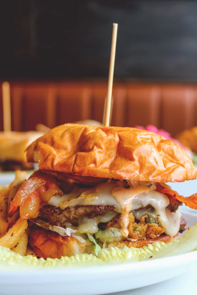 Stacked burger with cheese, lettuce, bacon, and fries on a white plate.