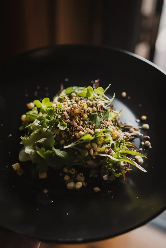 Vibrant salad with mixed greens, corn, and toasted seeds on black plate.