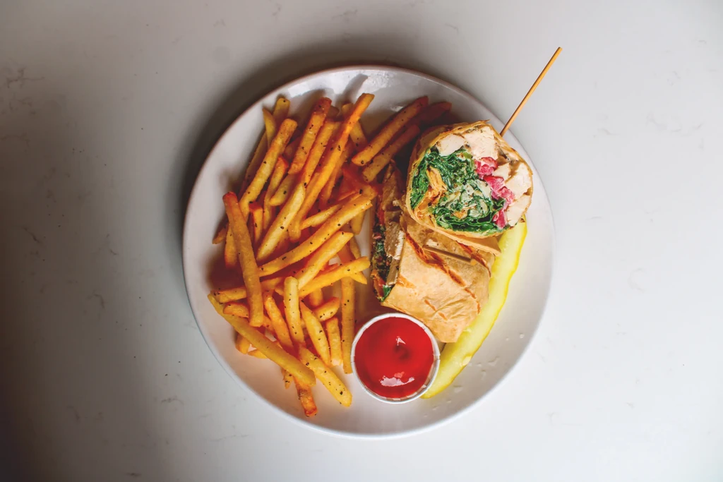 Plate of seasoned fries, cut wrap, ketchup, and pickle spear.