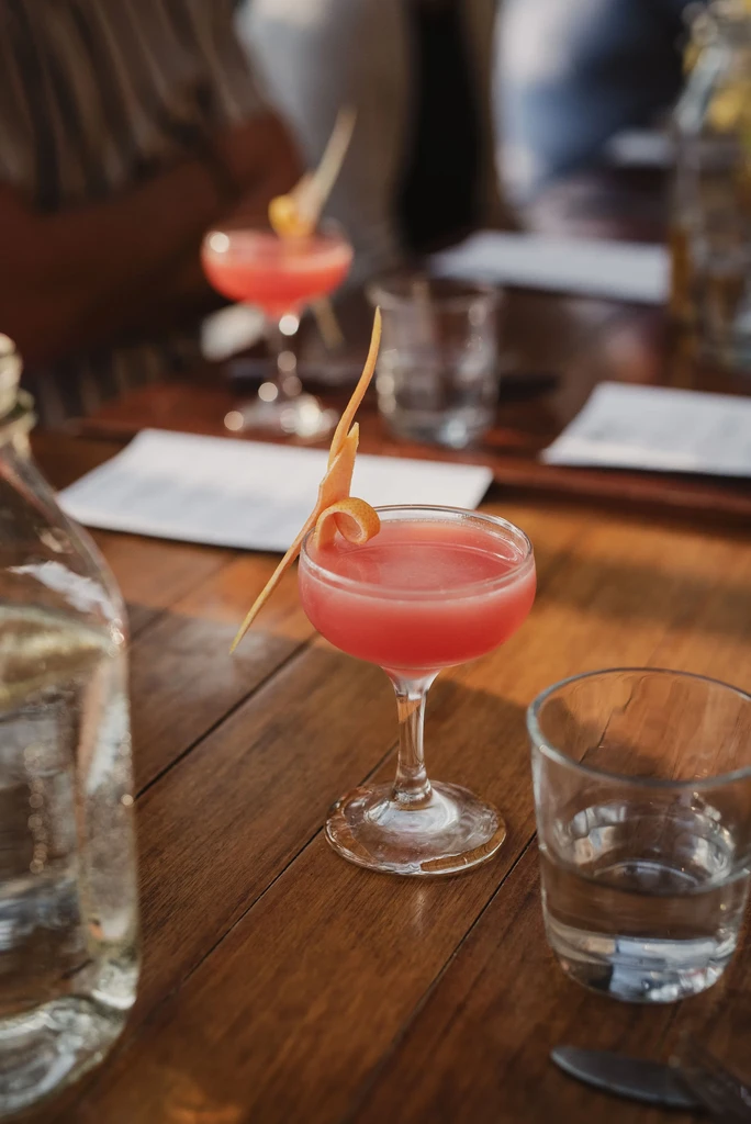 Reddish-pink cocktail in a coupe glass with citrus peel.