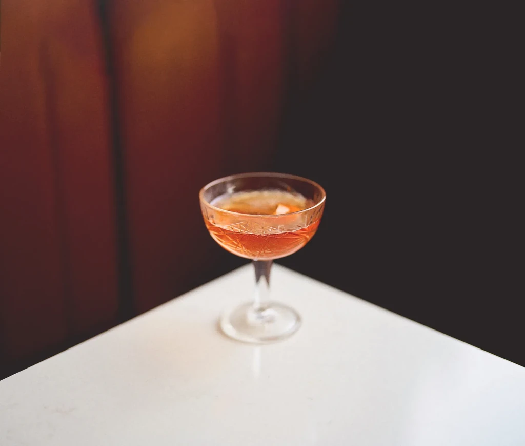 Vintage coupe glass with reddish-orange cocktail and citrus garnish.