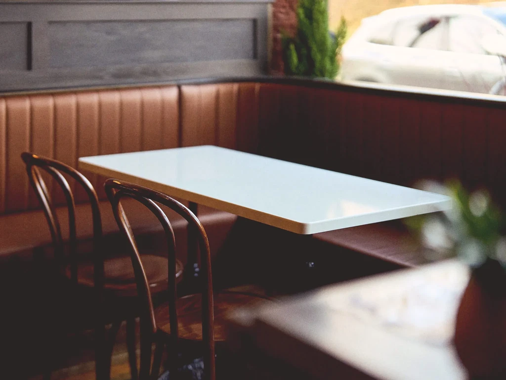 Restaurant booth with tufted brown leather, white table, two dark chairs.