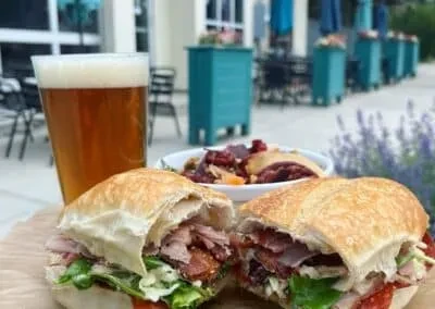 Hearty sandwich, foamy beer, and colorful side dish on outdoor patio.