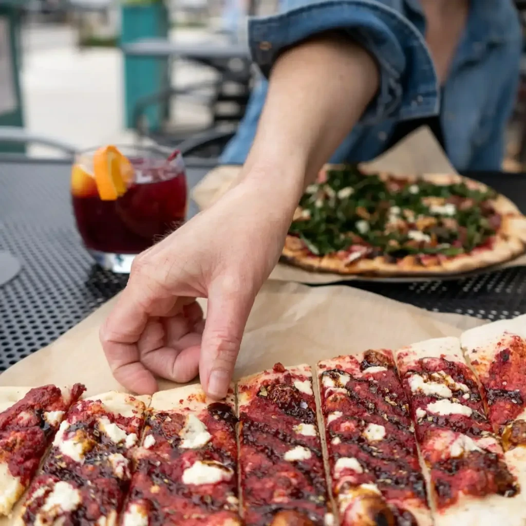 Hand picking a slice of red sauce pizza from an outdoor table.