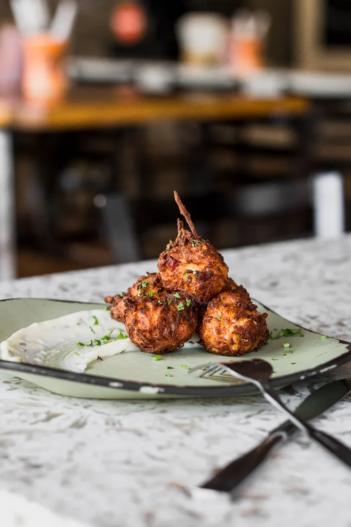 Golden-brown fried croquettes with white sauce and herbs on a green plate.