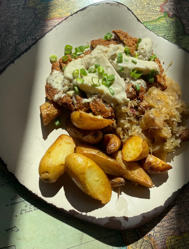 Crispy cutlet with sauce, shredded cabbage, and potatoes on vintage map background.