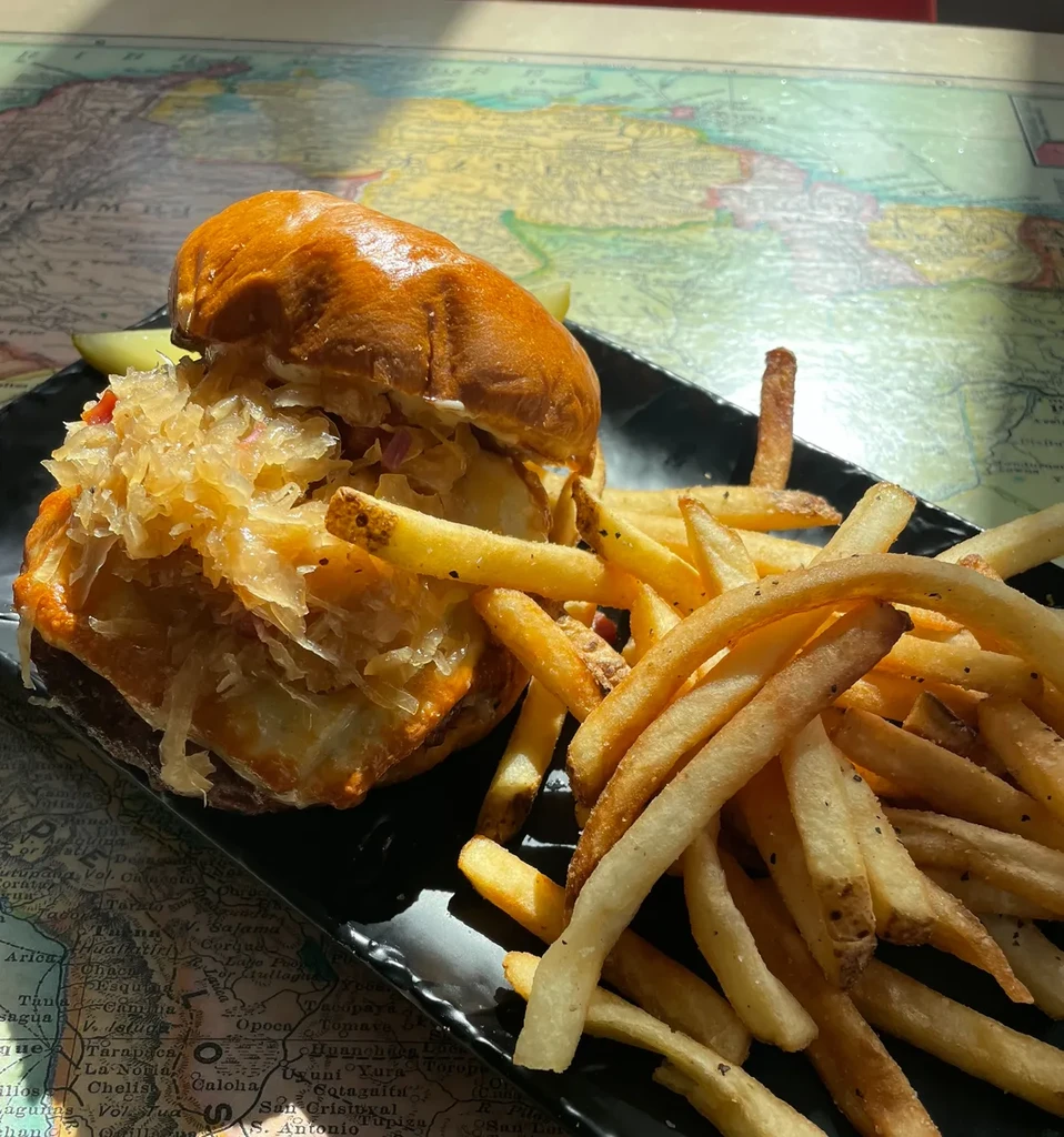 Sauerkraut sandwich, fries, and pickle on a world map table.