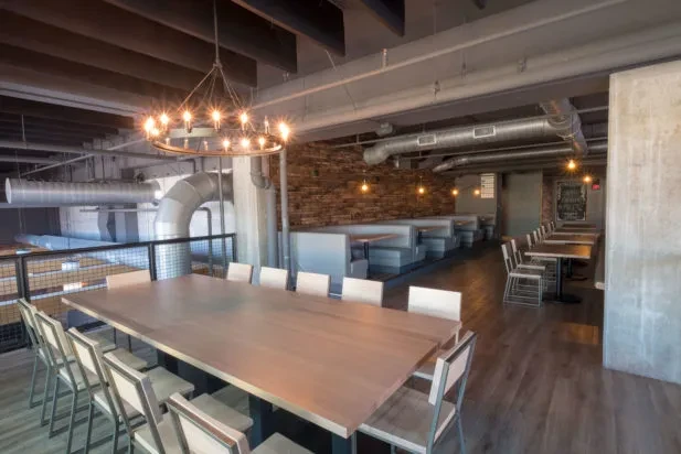 Empty modern restaurant interior with industrial-chic design, communal table, and ductwork.