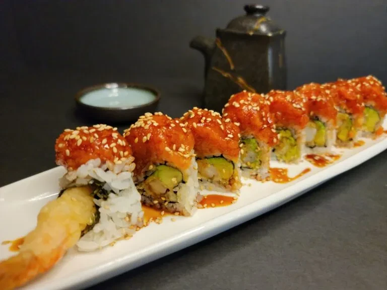 Eight sushi rolls with orange topping, avocado, shrimp, and sesame.