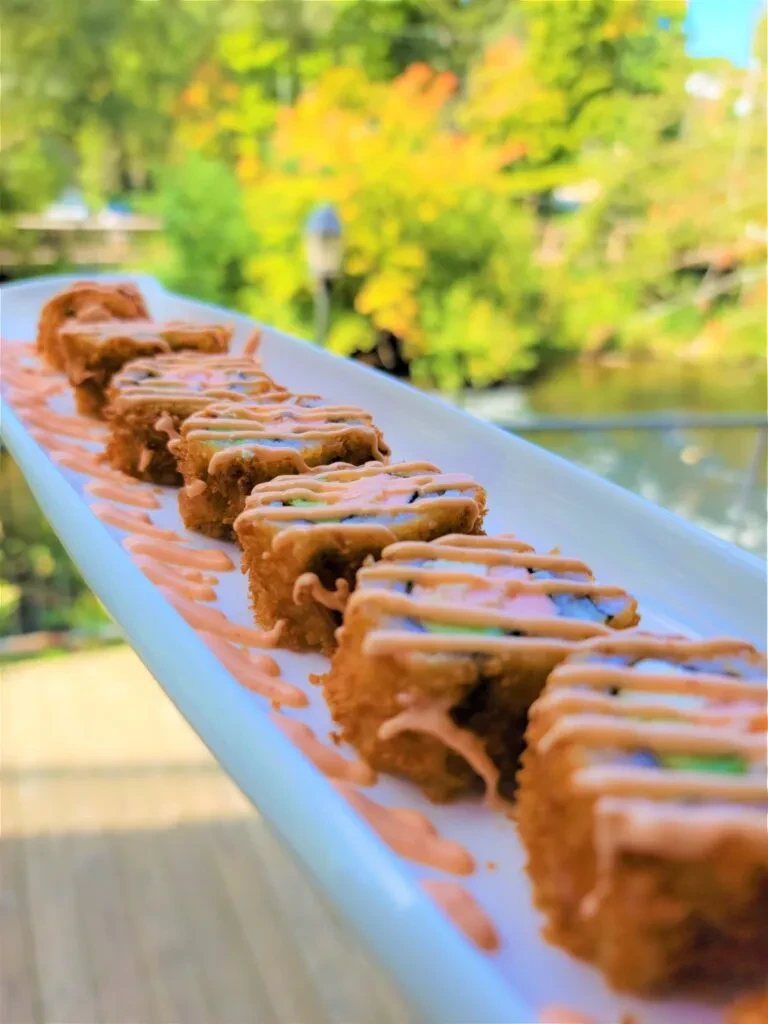Crispy deep-fried sushi rolls with sauce, blurred autumn background.
