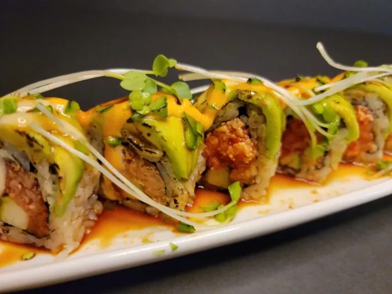 Eight avocado-topped sushi rolls with orange sauce on a white plate.