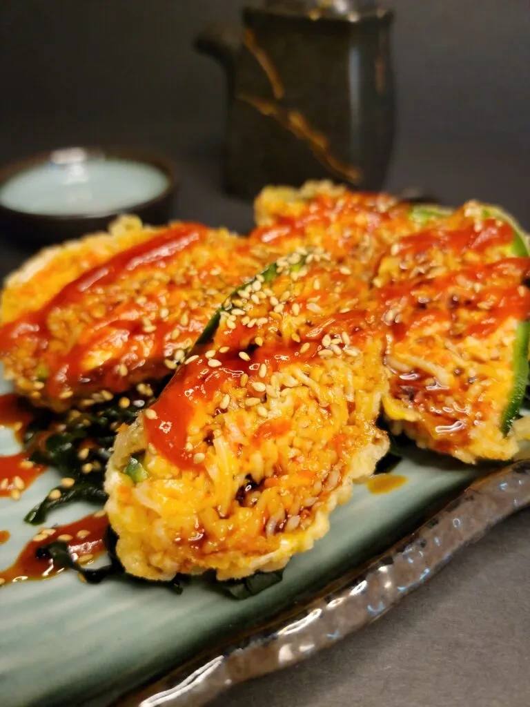 Crispy tempura pieces with red sauce, sesame, rice, and seaweed salad.
