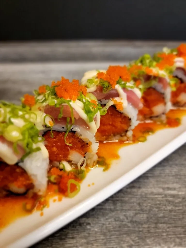 Sushi rolls garnished with tuna, tobiko, green onions, and two sauces.