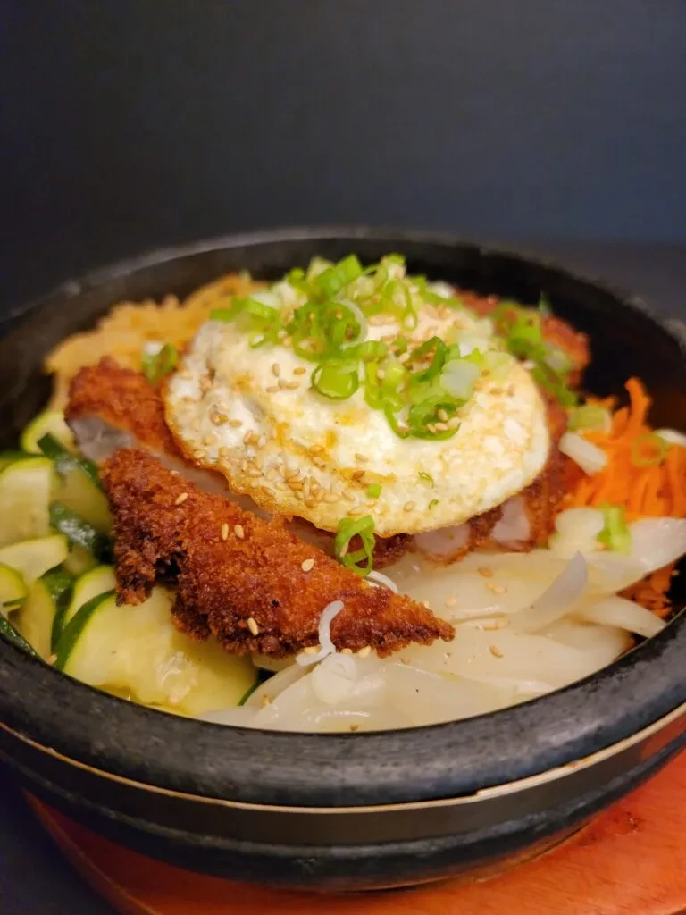 Vibrant stone pot bibimbap with fried egg, cutlet, and vegetables.