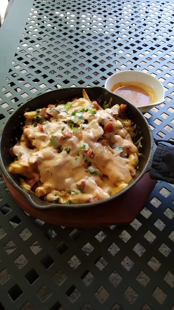 Loaded fries in a cast iron skillet with cheese, tomatoes, onions.