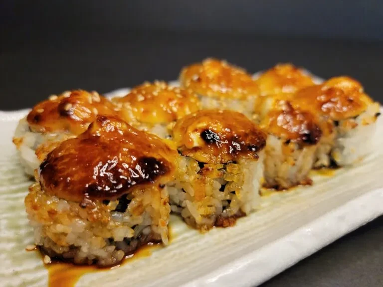 Eight baked sushi rolls with glossy golden sauce and sesame seeds.