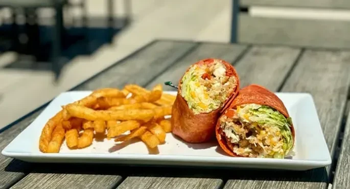 Halved wrap, colorful filling, and golden crinkle fries on a white plate.