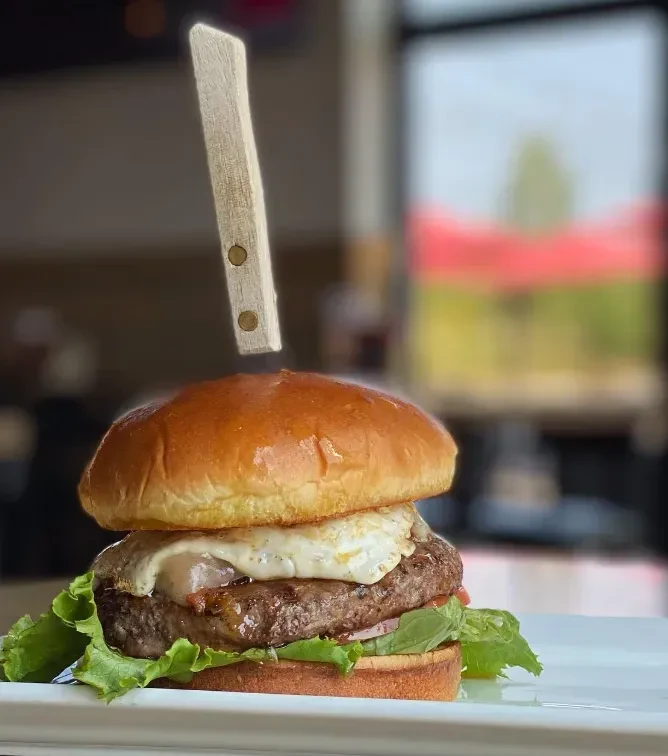 Gourmet burger with brioche bun, beef patty, melted cheese, lettuce, knife.