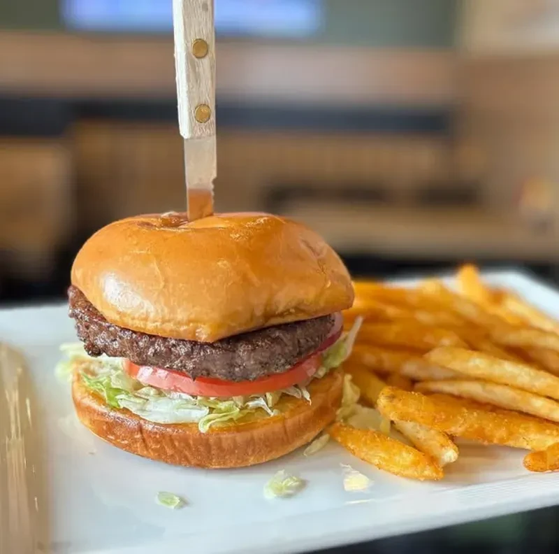 Burger with knife, lettuce, tomato, and fries on a white plate.