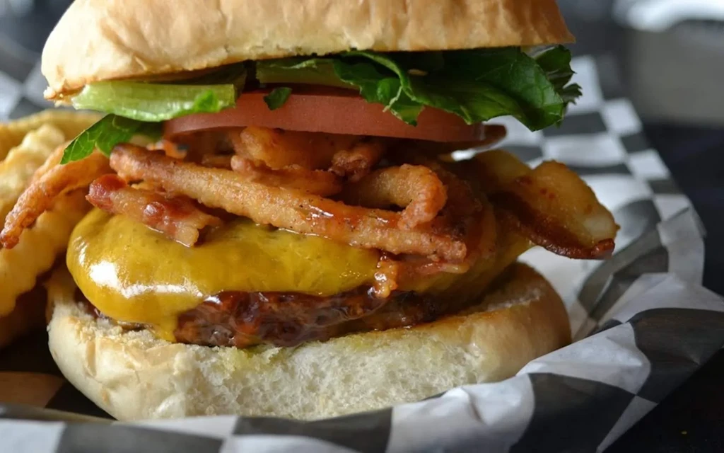 Gourmet burger with cheese, bacon, onions, tomato, lettuce, and fries.