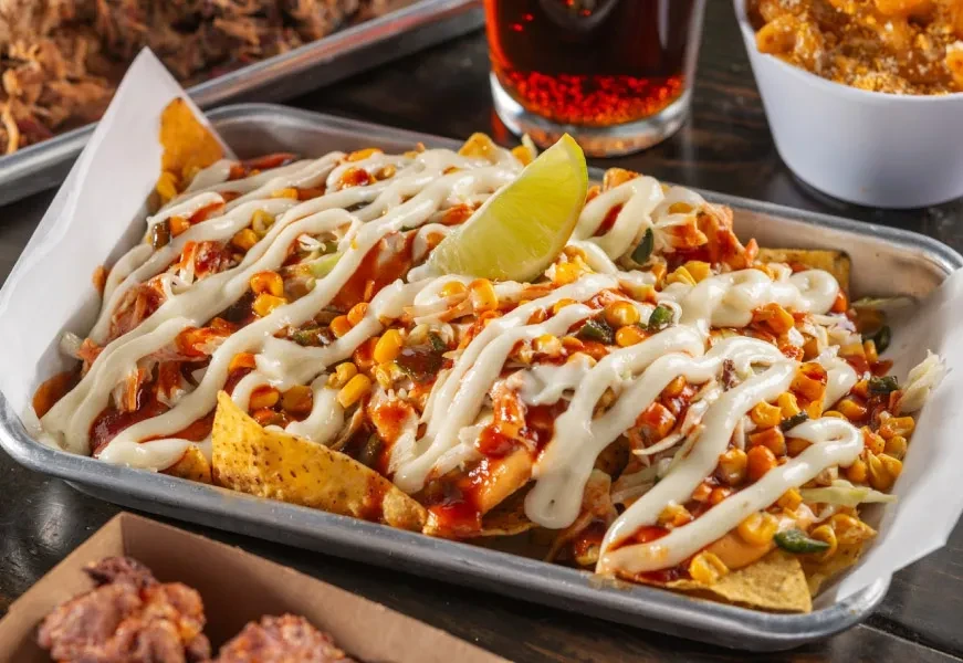 Loaded nachos in a metal tray with meat, sauces, and a lime.