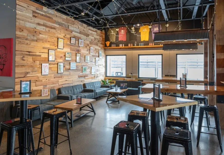 Empty modern industrial restaurant with rustic wood, exposed pipes, and seating.