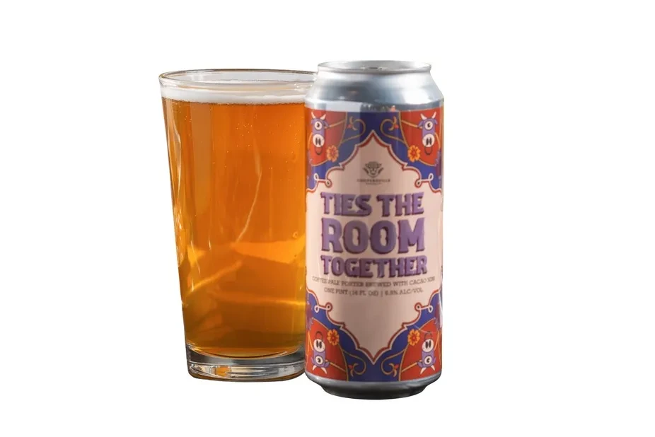Pint glass of beer next to a 'Ties The Room Together' can.
