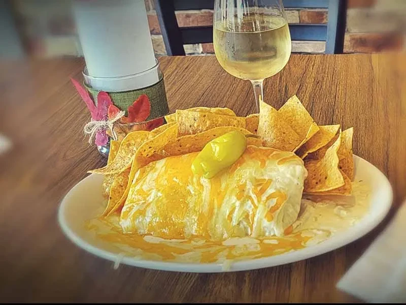 A generously sauced dish with melted cheese, a pepper, and tortilla chips.
