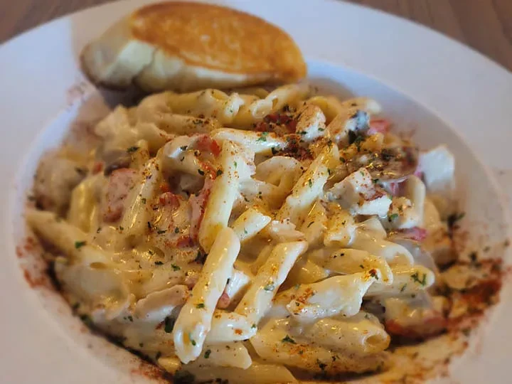 Creamy penne pasta with chicken, red pieces, herbs, spice, and bread.