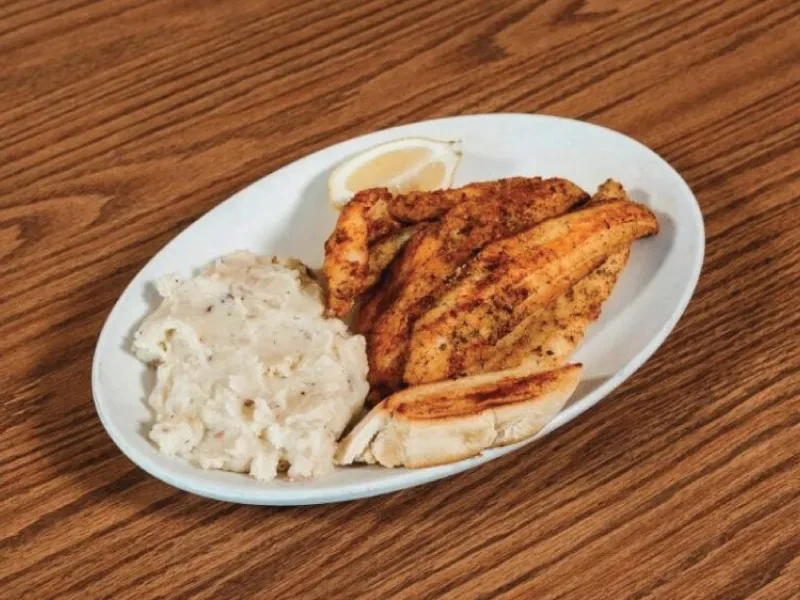Seasoned grilled fish, mashed potatoes, and lemon on a white plate.