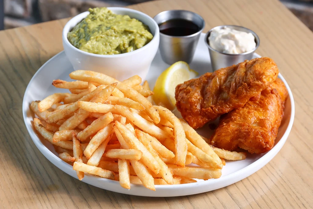 Well-presented fish and chips with lemon, mashed peas, and sauces.