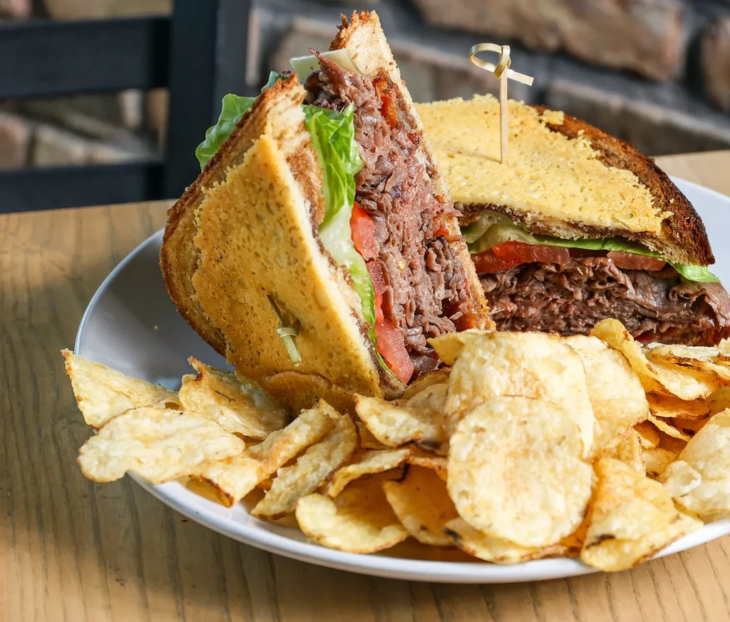 Roast beef club sandwich halves with melted cheese and potato chips.