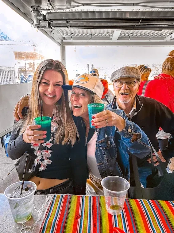 Two women and a man hold colorful drinks on an outdoor patio.