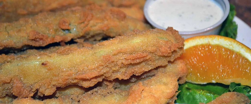 Crispy fried items with herb dipping sauce, garnished with an orange slice.