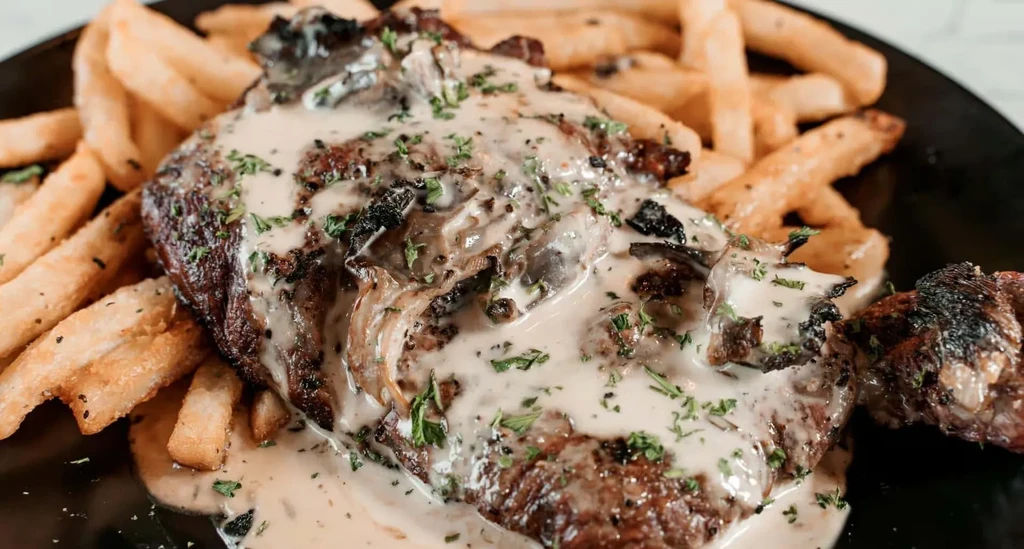 Seared steak with mushroom cream sauce, herbs, and golden fries.