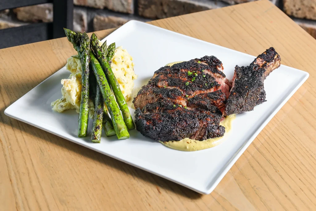 Professionally plated bone-in steak with mashed potatoes and asparagus.