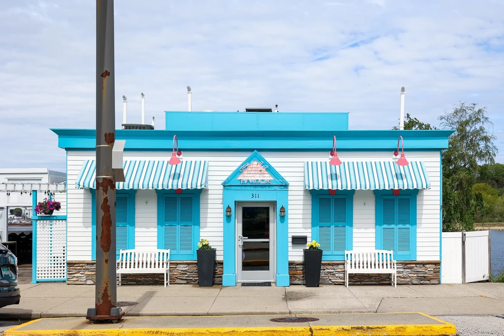 White building with turquoise trim, awnings, and 'Sweet Sixteen Harbor' neon sign.