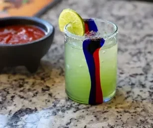 Vibrant green cocktail with blue, red streaks, lime, and salsa.