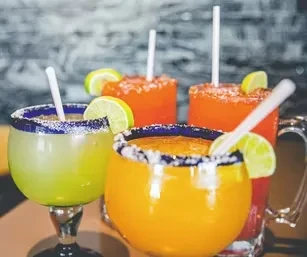 Four colorful, frozen cocktails with lime wedges in assorted glasses.