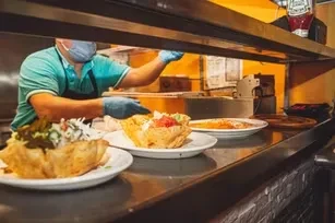 Worker in mask and gloves prepares three meals in edible bowls.