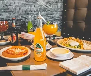 Restaurant table with Jarritos soda, beer, cheesy enchiladas, and a quesadilla.