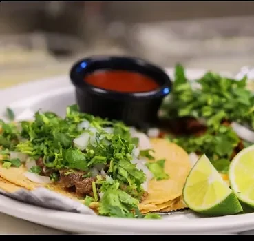 Tacos topped with cilantro and onions, served with lime and salsa.