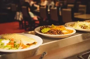 Plates of various Mexican foods on a stainless steel buffet.