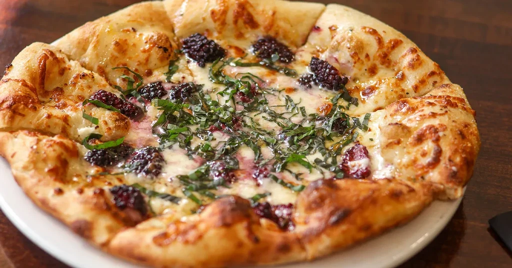 Baked pizza with melted white cheese, blackberries, and green herbs.