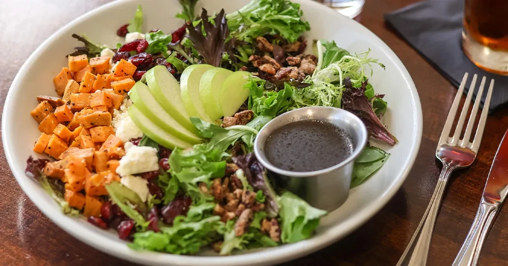 Vibrant salad with greens, sweet potato, feta, apple, pecans, and dressing.