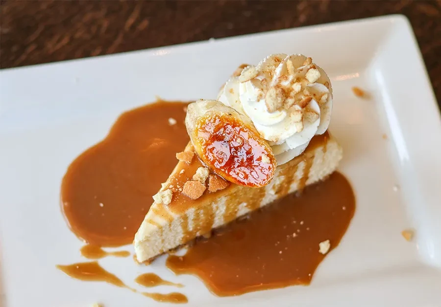 Cheesecake slice with caramel, whipped cream, nuts, and caramelized banana.