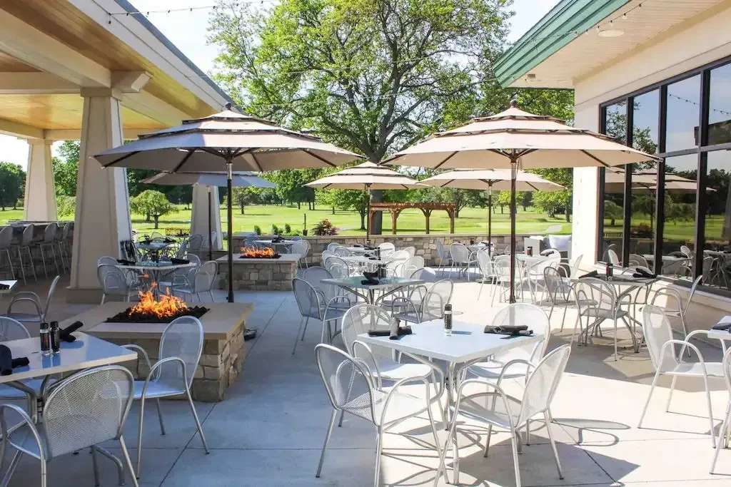 Restaurant patio with dining tables, fire pits, umbrellas, and green landscape.